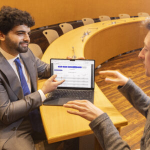 K5125 Sam Hieken in Joslin Senate Chamber Two men sit at a conference table and review information on a laptop.
