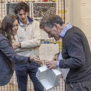 F0425 Alumni Traveling Studio Final Review Two people inspect a 3D architectural model held by a third person at a conference.
