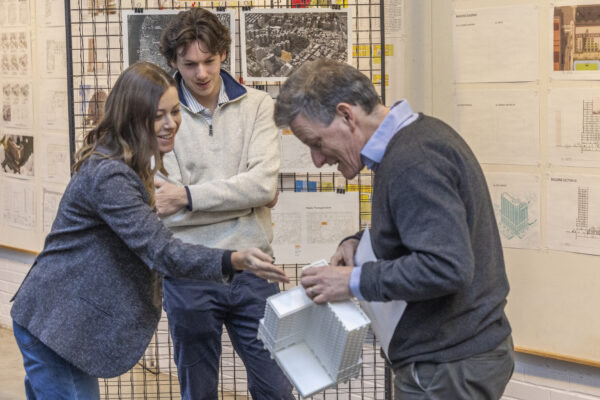 F0425 Alumni Traveling Studio Final Review Two people inspect a 3D architectural model held by a third person at a conference.
