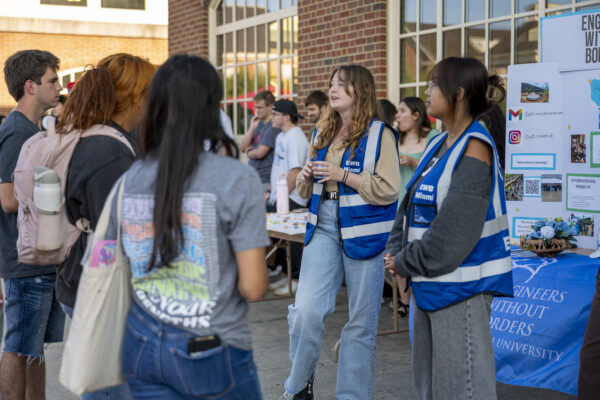 Q0226 CEC Party on the Patio Two Engineers without Borders volunteers talk to an interested crowd gathered around a poster board display.
