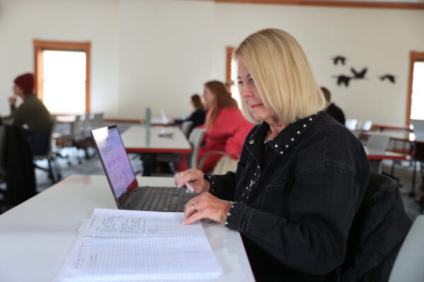 K11226 Debra Saunders Brown news story An older woman works on her laptop while looking at her notes.